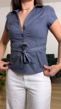 Γυναίκα με εφαρμοστό μπλε μπλουζάκι με κοντά μανίκια, ζώνη με πουά σχέδιο στη μέση και λευκό παντελόνι, προσαρμόζοντας το τελείωμα της μπλούζας σε εσωτερικό χώρο.