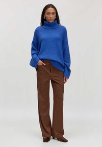 Blauer oversized Strickpullover mit hohem Kragen und gerippten Bündchen, kombiniert mit braunen weiten Hosen und spitzen Schuhen. Einfaches, strukturiertes Design.