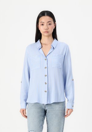 Camicia azzurro chiaro con righe verticali bianche e gialle, due tasche sul petto e maniche lunghe con risvolto. Tessuto morbido.