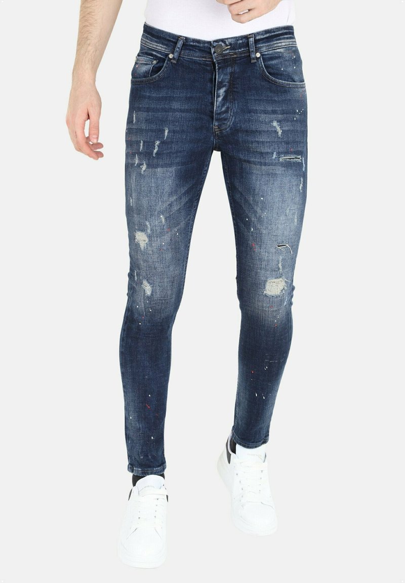 Skinny-fit denim jeans in vervaagd blauw, met verwerkte details en verfsplatschade. Vijf-pocket ontwerp met metalen hardware en gestikte naden.