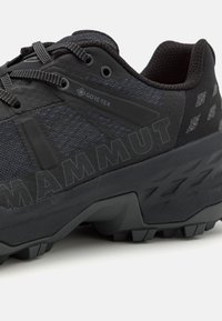Chaussure de randonnée noire avec tige en mesh texturé, étiquette Gore-Tex, semelle en caoutchouc épaisse et marquage "MAMMUT" bien visible sur le côté.