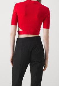 Top corto rojo con mangas cortas, que presenta un escote en la espalda y una banda de tela. Combinado con pantalones negros de corte entallado. Textura suave.