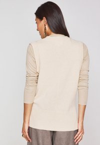 Maglione beige a maglia con maniche lunghe, polsini a coste e una texture liscia, con schiena dritta e un orlo leggermente più lungo.