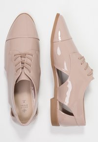 Chaussures en cuir verni rose clair avec un bout pointu, design à lacets et côtés découpés. Semelle plate en caoutchouc beige pour le confort.