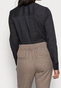 Black long-sleeve shirt with a smooth texture, paired with brown houndstooth patterned trousers featuring an elastic waistband and side pockets.