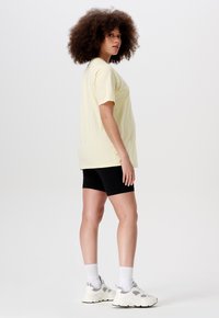 Geel T-shirt met korte mouwen gecombineerd met zwarte shorts. Model draagt witte sneakers met grijze accenten en geribbelde crew-sokken. De textuur lijkt zacht.