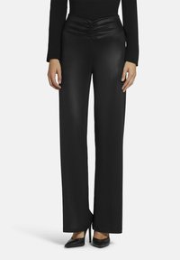 Zwarte wijde broek met een gerimpelde tailleband, gemaakt van een gladde stof. In combinatie met puntige zwarte hakken. Eenvoudig en gestroomlijnd ontwerp.