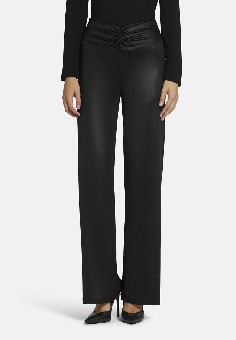 Zwarte wijde broek met een gerimpelde tailleband, gemaakt van een gladde stof. In combinatie met puntige zwarte hakken. Eenvoudig en gestroomlijnd ontwerp.