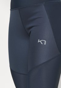 Leggings blu navy realizzati in tessuto elasticizzato, con cuciture flat e un design con pannelli diagonali. Un piccolo logo grigio è visibile sulla gamba.