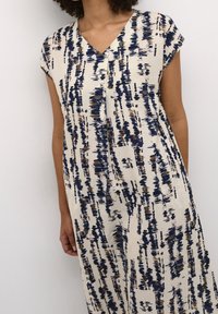 Robe col en V à manches courtes volantées, avec un fond crème orné de motifs abstraits bleu et brun, confectionnée en tissu léger.