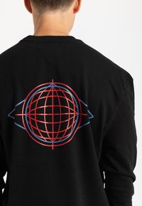 Black long-sleeve shirt featuring a graphic design of a globe in red and blue lines on the back, with a smooth fabric texture.
