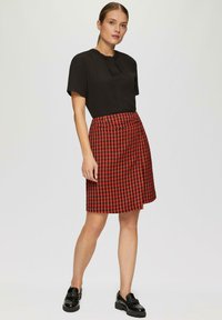 Zwart T-shirt met korte mouwen en een geplooide halslijn; rok met een rood patroon en een houndstooth ontwerp; gedragen met zwarte instappers.