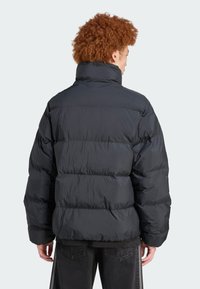 Must must jacket kõrge kraega, millel on tikitud disain, elastsed mansetid ja laia lõikega. Sile, läikiv materjal on nähtavalt kortsus.