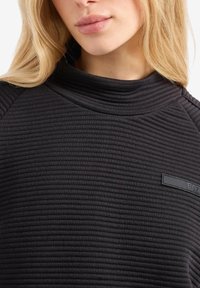 Felpa nera con texture, dotata di un alto colletto, design a coste e un discreto logo ricamato sulla parte frontale. Tessuto morbido con un look aderente.