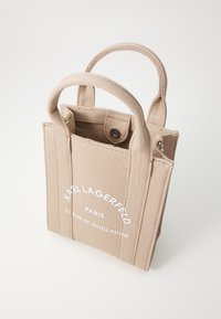 Beige lerret tote bag med to korte håndtak. Har hvit trykket tekst: "KARL LAGERFELD PARIS 21 RUE ST-GUILLAUME." Kompakt rektangulær form.