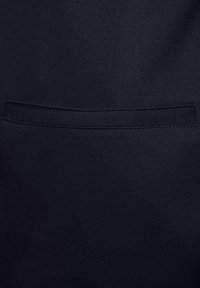 Námořnická modrá bavlněná látka s hladkou texturou, na které je našitá horizontální kapsa. Bez viditelných vzorů nebo kovových prvků.