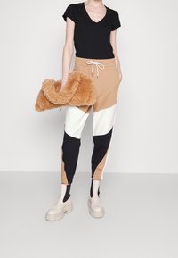 Černé tričko s výstřihem do V, joggers v tan a černé barvě s elastickými manžetami a krémové platformové boty. Modelka drží chlupatou béžovou kabelku.