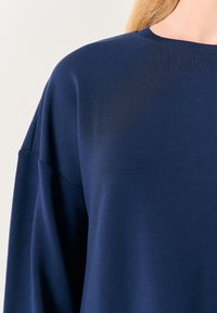 Maglia a maniche lunghe di colore blu navy realizzata in un morbido cotone misto, con scollatura a girocollo e cuciture delle spalle ribassate per una vestibilità rilassata.