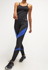 Svart atletisk linne i kombination med svarta leggings med blå diagonala detaljer och mesh-paneler, kompletterat med svarta träningsskor.