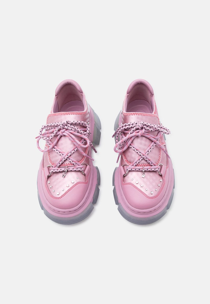Klumpige pinke Sneaker mit dicken grauen Sohlen, gemusterten Schnürsenkeln, die zu Schleifen gebunden sind, und silbernen Nieten im Zehenbereich, von oben auf einem weißen Hintergrund gezeigt.
