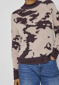 Pull en maille floue beige avec un motif abstrait violet foncé, col rond, et ourlets et poignets côtelés. Associé à un jean bleu.