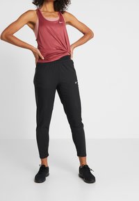 Bordowy sportowy top bez rękawów z supełkiem, zestawiony z czarnymi, zwężanymi dresami z siateczkowymi wstawkami i elastycznym paskiem w talii. Czarne sneakersy.