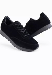 Musta mokkanahkasandaalit, joissa on pyöristetyt varpaat, litteät nauhakengät ja kuvioitu kumipohja, joissa on sileät yksityiskohdat sivuilla.