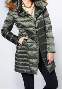 Abrigo acolchado color verde oliva con cremallera frontal, patrón acolchado horizontal y capucha con piel sintética. Cuenta con bolsillos laterales con detalles en herrajes dorados.
