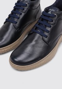 Zapatos de piel azul marino con un acabado liso, featuring cordones azul marino, puntera redondeada y suela de goma beige texturizada. Diseño moderno y minimalista.