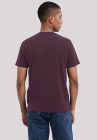 Maroon cotton T-shirt with a crew neck and short sleeves, viewed from the back. Paired with blue denim jeans. Simple design, no patterns.