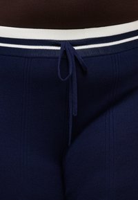 Μπλε ναυτικό πλεκτό παντελόνι με λωρίδα ελαστική μέση σε λευκό και μπλε ναυτικό και δεμένη κορδονάκι στο μπροστινό μέρος.