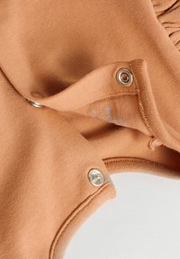 Vêtement en coton marron clair avec des boutons-pression et une texture lisse. Présente un col légèrement côtelé et un détail d'étiquette intérieure.