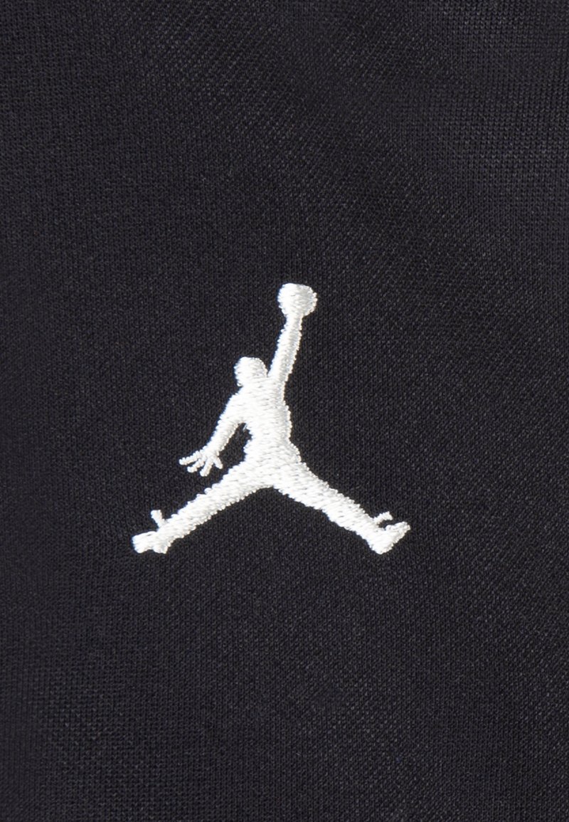 Logo Jumpman ricamato bianco su tessuto nero, che raffigura il contorno di una persona che salta per tirare a canestro. Design semplice e pulito.