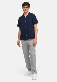 Camisa de marinero de manga corta con cuello abotonado, tejido texturizado, combinada con pantalones gris claro y zapatillas blancas. Modelo de pie.