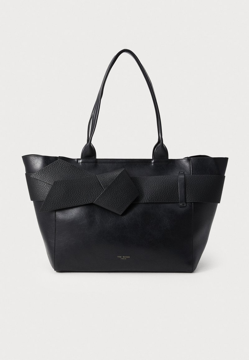 Sac fourre-tout noir en cuir texturé, présentant un imposant détail de nœud géométrique, des poignées doubles et une silhouette structurée.