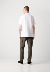 Hvit polo skjorte, kort erme, rett snitt. Olivengrønne cargo bukser med sidelommer, elastiske mansjetter, og svarte joggesko med hvite såler.