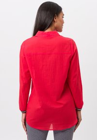 Rode blouse met lange mouwen en een kraag, gemaakt van een lichtgewicht stof en met een gebogen zoom. Inclusief contrasterende zwart-witte accenten op de mouwen.
