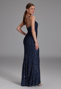 Robe de soirée en sequins bleu marine avec une silhouette ajustée, dotée de bretelles spaghetti et d'un dos nu, s'étendant jusqu'au sol.