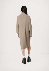 Abito in maglia beige a coste con collo alto e maniche lunghe, che arriva a metà polpaccio. Indossato con calzini bianchi e scarpe nere con tacco.