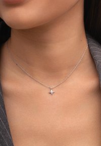 Collar de plata con una cadena delicada y un colgante en forma de estrella que presenta una gema central, sobre un tono de piel neutro.