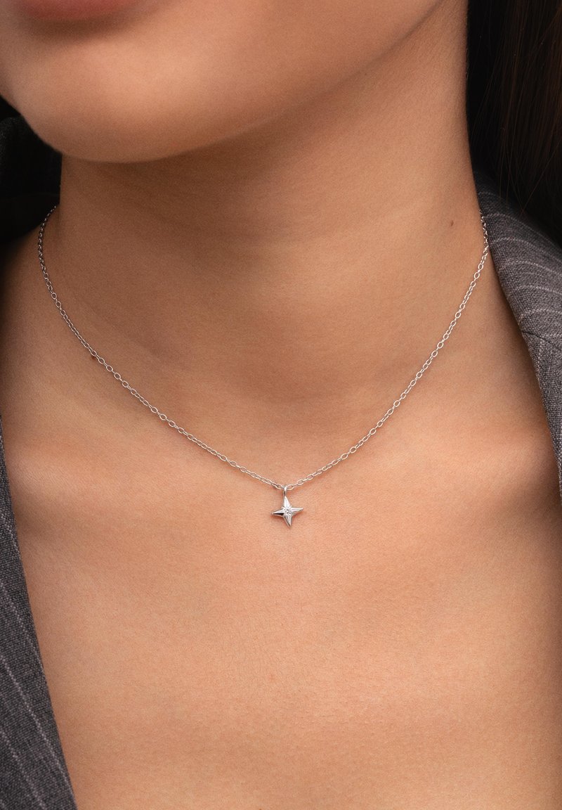 Collar de plata con una cadena delicada y un colgante en forma de estrella que presenta una gema central, sobre un tono de piel neutro.