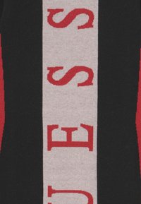 Pletený svetr s výrazným grafickým vzorem v červené a světle šedé barvě, s alternujícími černými sekcemi. Design obsahuje velké písmo.