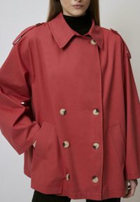 Giacca rossa, oversize, realizzata in un tessuto testurizzato, con un design doppiopetto, grandi bottoni e tasche laterali per funzionalità.