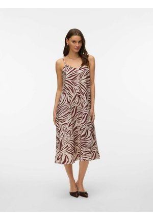 Femme portant une robe sans manches arrivant aux genoux avec des rayures zébrées bordeaux et beige, associée à des chaussures noires à bouts pointus et des boucles d'oreilles en perles.