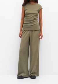 Haut en tricot côtelé vert olive avec des manches courtes et un détail froncé, associé à un pantalon large assorti. Présente une texture douce et un ajustement confortable.