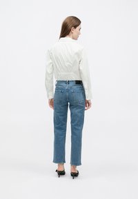 Balti marškiniai su klosčių detalėmis nugaroje, derinami su mėlynais tiesaus kirpimo džinsais su užpakalinėmis kišenėmis ir juodais aukštakulniais bateliais.