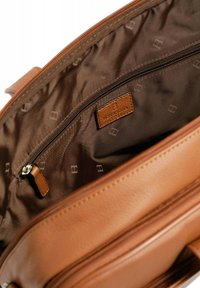 Interieur van een bruine lederen tas met een gladde textuur, een ritsvak en een merklabel tegen een effen bruine voering met subtiele patronen.