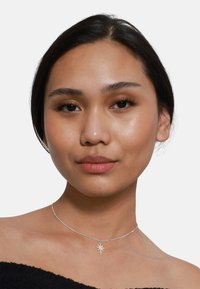 Collana choker in argento con pendente a forma di stella, caratterizzata da una delicata catena e una finitura liscia e lucida. Design semplice ed elegante.