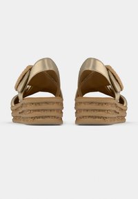 Paire de sandales compensées dorées avec semelles plateformes beige texturées vues de dos sur un fond clair uni.