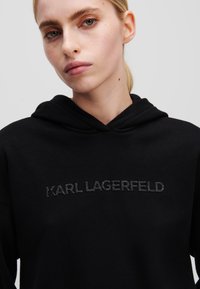 Zwarte hoodie van zacht materiaal, met een verhoogd, geborduurd logo "KARL LAGERFELD" in donkere draad over de borst. Gedurfde, pullover ontwerp.